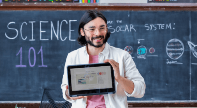 Photo of teacher holding tablet in front of blackboard