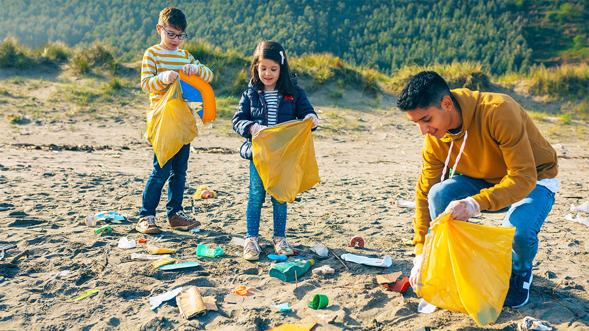 Three children picking up trash on the beach