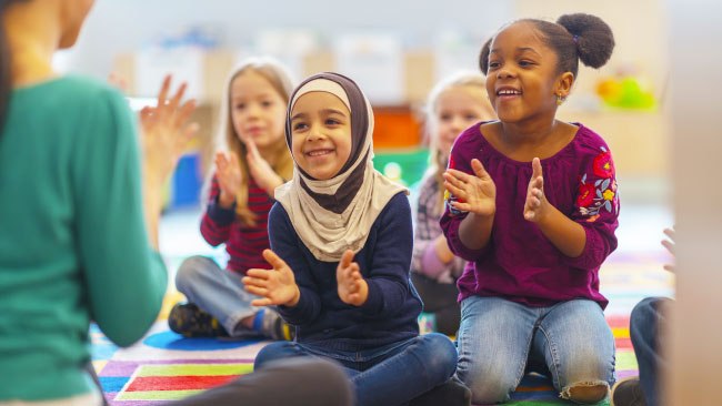 Des élèves de différentes cultures applaudissent avec un enseignant dans une salle de classe